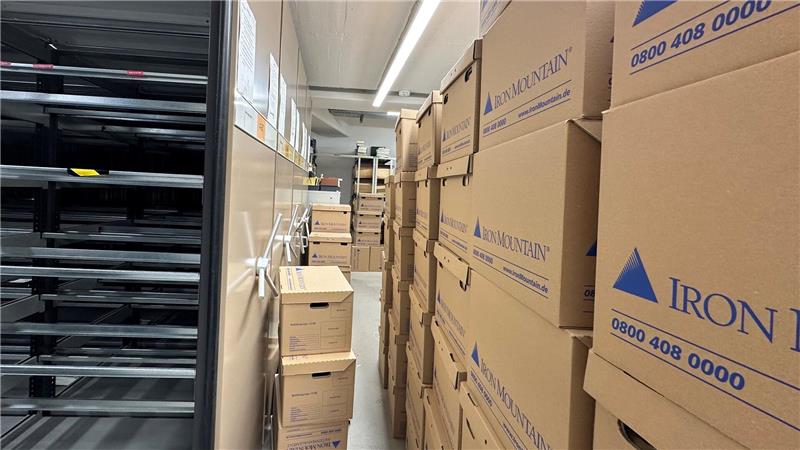 Akten lagern in Umzugskartons. Daneben sind leere Aktenschränke zu sehen.