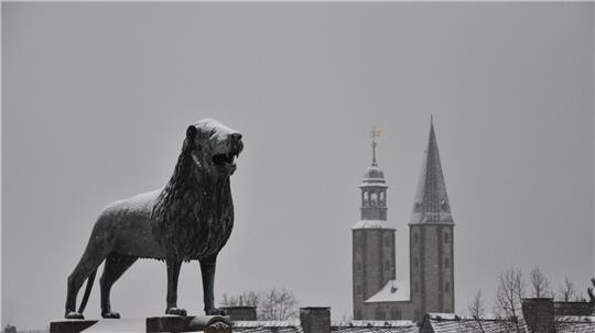 Eine Statue in Form eines Löwen steht vor einem Kirchturm.