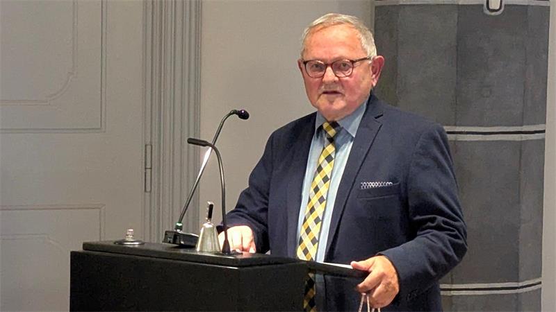 Ein älterer Mann mit grauem Haar und Brille steht hinter einem schwarzen Rednerpult und spricht in ein Mikrofon