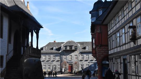 Historisches Fachwerkhaus mit geschwungenem Dach und mehreren Fenstern, umgeben von weiteren Fachwerkgebäuden unter blauem Himmel.