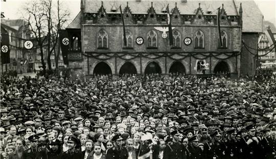 Große Menschenmenge vor einem historischen Gebäude mit mehreren Hakenkreuz-Symbolen an der Fassade