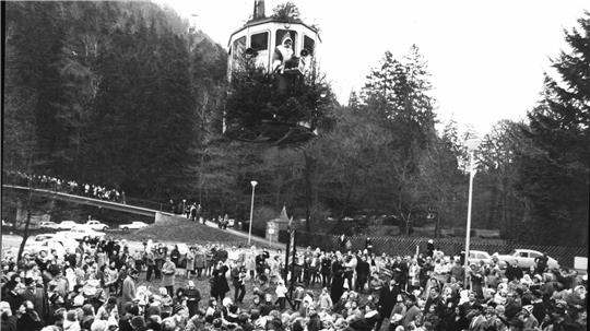 Eine Menschenmenge erwartet in den 1960ern den Nikolaus, der mit der Burgbergseilbahn vom Bad Harzburger Burgberg kommt. Auf dem Bild schwebt die dekorierte Bergbahngondel über vielen Kindern, der Nikolaus schaut aus dem Fenster der Gondel und winkt.  
