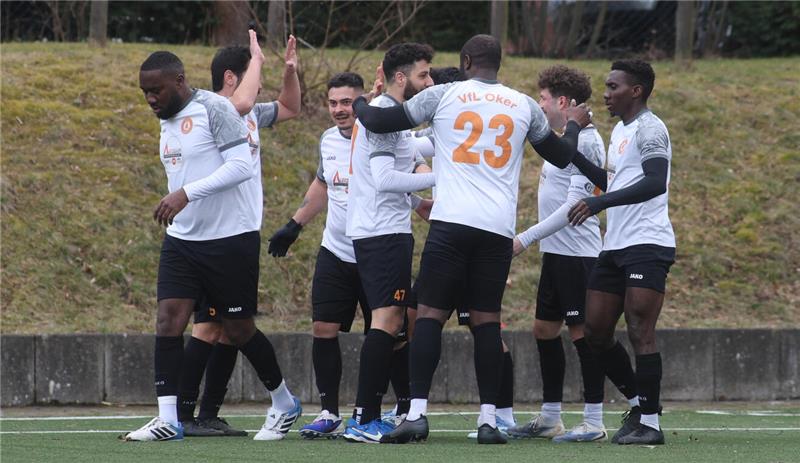 Fußballspieler in weißen Trikots mit schwarzen Hosen stehen auf einem Spielfeld und geben sich gegenseitig High-Fives