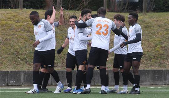 Fußballspieler in weißen Trikots mit schwarzen Hosen stehen auf einem Spielfeld und geben sich gegenseitig High-Fives