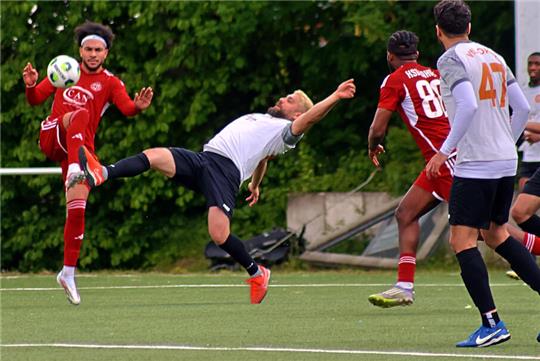 Fußballspieler in Aktion auf dem Spielfeld, einer führt einen Fallrückzieher aus, andere beobachten oder bewegen sich in Richtung Ball