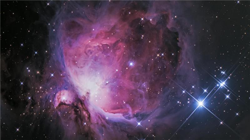 Nahaufnahme einer farbigen Nebelwolke mit mehreren hellen Sternen vor schwarzem Hintergrund