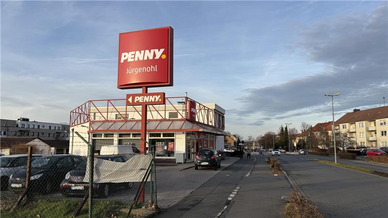 Supermarkt Penny mit rotem Logo auf großem Schild und Gebäude, mehrere geparkte Autos davor, Wohnhäuser im Hintergrund.
