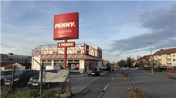 Supermarkt Penny mit rotem Logo auf großem Schild und Gebäude, mehrere geparkte Autos davor, Wohnhäuser im Hintergrund.