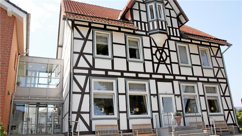 Fachwerkhaus mit weißer Fassade und dunklen Holzbalken sowie einem modernen Glasanbau auf der linken Seite.
