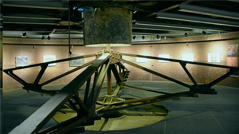 Innenraum mit großem, radial angeordnetem Metallrad und beleuchteten Bildern an den Wänden