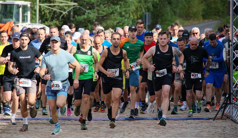 Gruppe von Läufern in Sportkleidung startet ein Rennen auf einem gepflasterten Weg vor einem Wald