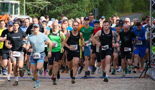 Gruppe von Läufern in Sportkleidung startet ein Rennen auf einem gepflasterten Weg vor einem Wald