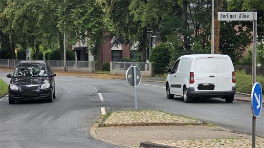 Zwei Fahrzeuge fahren auf einer Straße mit Mittelinsel und Straßenschild 'Berliner Allee'