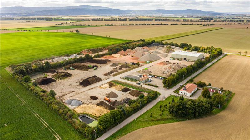 Goslarer Millionen-Deal: Schwenke de Wall verkauft an Bettels Luftaufnahme eines Betriebshofes mit mehreren Sand- und Kieshaufen, umgeben von Feldern und einzelnen Gebäuden.