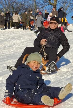 Zwei Personen rodeln eine Schneepiste hinab.