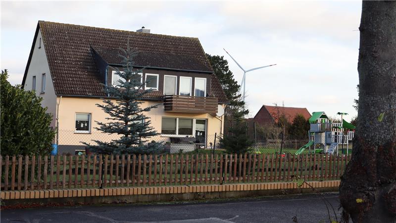 Zweistöckiges Haus mit braunem Dach hinter einem Holzzaun und einem Nadelbaum im Vorgarten
