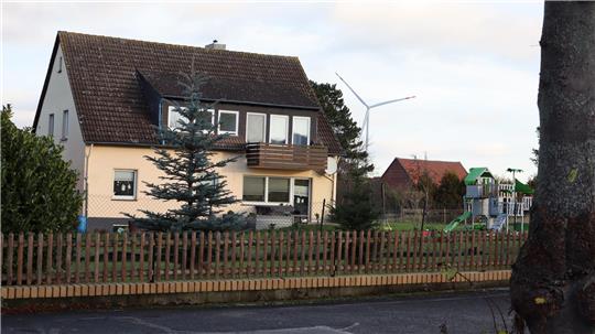 Zweistöckiges Haus mit braunem Dach hinter einem Holzzaun und einem Nadelbaum im Vorgarten