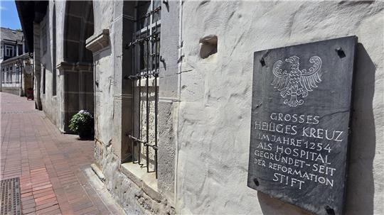 Steintafel mit Adlerrelief und Inschrift an einer historischen Mauer neben einem gepflasterten Gehweg in einer Altstadt