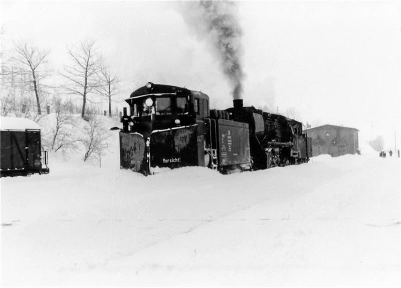 Der Schneepflug, von einer Dampflok geschoben, räumt das Gleis frei.