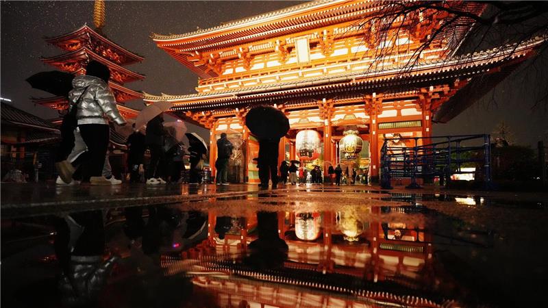 Der Sensoji-Tempel spiegelt sich in einer Pfütze, als Menschen zum Neujahrsgebet in Tokio ankommen.