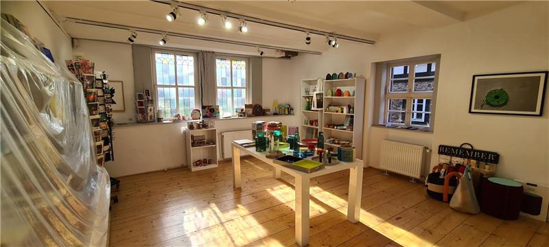 Blick in einen hellen Raum mit bunten Gegenständen, in den Lampen- und Sonnenlicht scheint. Links verhüllt eine durchsichtige Plane ein Regal.