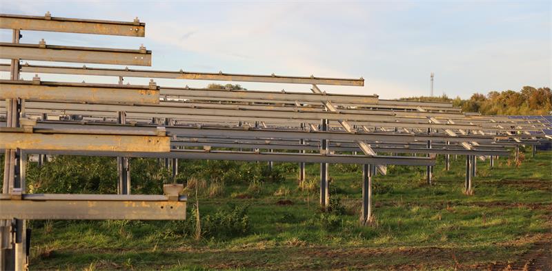 Weitläufige Solaranlage mit mehreren Reihen von Solarmodulen auf Metallgestellen in einer grünen Wiese unter klarem Himmel