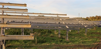 Weitläufige Solaranlage mit mehreren Reihen von Solarmodulen auf Metallgestellen in einer grünen Wiese unter klarem Himmel