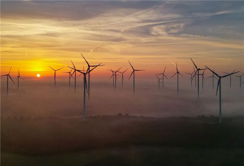 Der Sonnenaufgang scheint durch den Morgennebel über einem Windenergiepark.