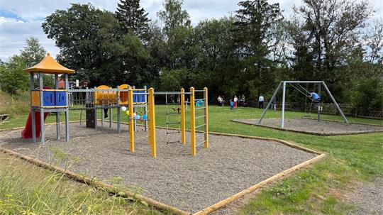 Kinder Spielen auf einem Spielplatz. Zu sehen ist unter anderem ein Klettergerüst und eine Schaukel.