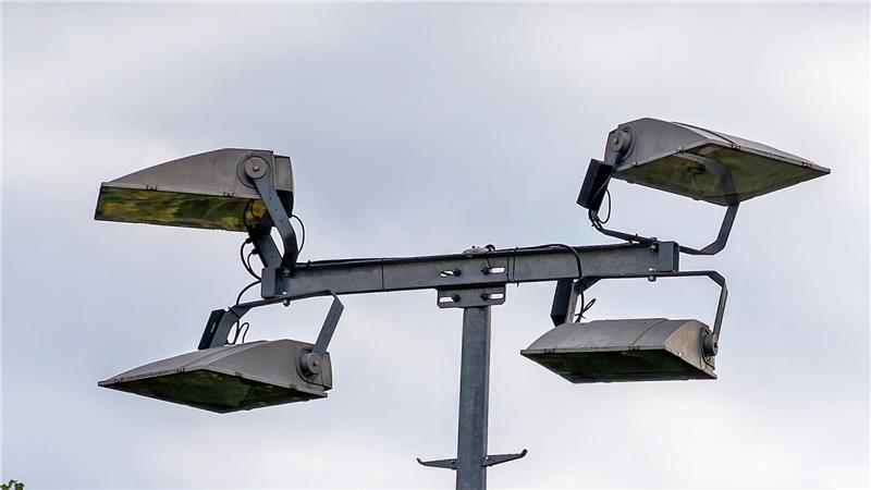 Vier große, rechteckige Flutlichtstrahler an einem Metallmast vor bewölktem Himmel.