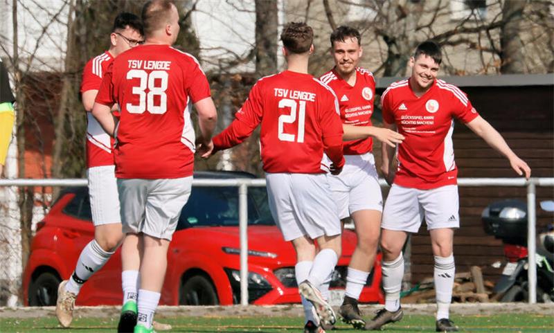 Fußballspieler in roten Trikots mit der Aufschrift "TSV LENGDE" und weißen Hosen feiern auf einem Spielfeld,