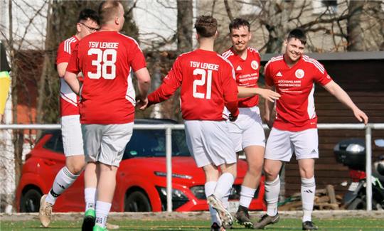 Fußballspieler in roten Trikots mit der Aufschrift "TSV LENGDE" und weißen Hosen feiern auf einem Spielfeld,