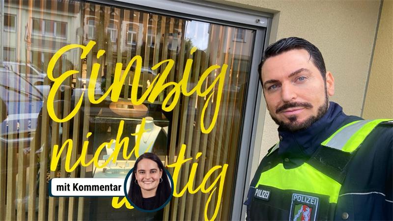 Polizist mit schwarzem Bart und kurz geschnittenem Haar in Uniform mit reflektierenden Streifen vor einem Schaufenster mit gelber Schrift 'Einzig nicht artig'.