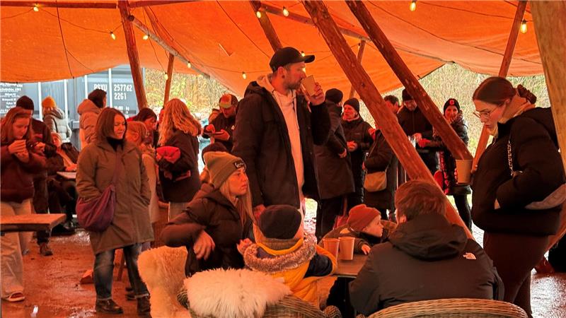 Dutzende von Besuchern gehen, stehen und sitzen in einem großen offenen Zelt.