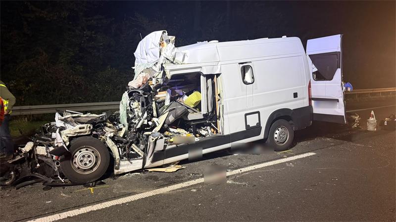 Schwer beschädigter weißer Transporter mit offener Hecktür auf einer Straße bei Nacht.