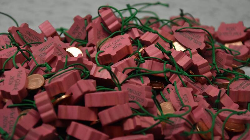 Viele rote Holzanhänger mit grünen Schnüren und kleinen Kupfermünzen liegen auf einer Oberfläche