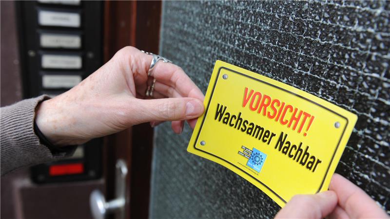 Eine Frau heftet einen Aufkleber der Polizei als Präventivmaßnahme zur Vorbeugung von Wohnungseinbrüchen an ihre Haustür.