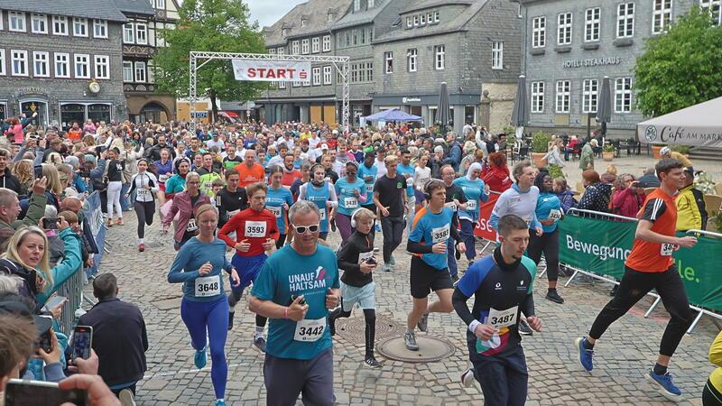 Läuferinnen und Läufer starten ein Straßenrennen vor historischen Fachwerkhäusern auf einem gepflasterten Platz mit Zuschauern am Rand
