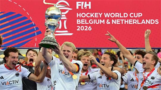 Männer-Hockeyteam jubelt, ein Spieler hält Pokal hoch, im Hintergrund Text 'FIH HOCKEY WORLD CUP BELGIUM & NETHERLANDS 2026'