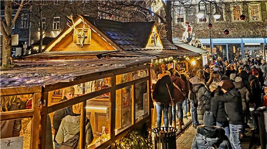 Weihnachtsmarkt mit beleuchteten Holzhütten und vielen Menschen in Winterkleidung bei Nacht.