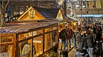Weihnachtsmarkt mit beleuchteten Holzhütten und vielen Menschen in Winterkleidung bei Nacht.