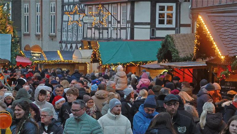 Große Menschenmenge auf einem Weihnachtsmarkt mit festlich geschmückten Ständen und beleuchteten Sternen in einer Altstadt.