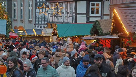Große Menschenmenge auf einem Weihnachtsmarkt mit festlich geschmückten Ständen und beleuchteten Sternen in einer Altstadt.