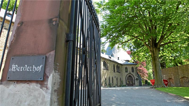 Eingangstor mit Schild ‚Werdehof‘ an einem historischen Gebäude mit Bäumen und gepflastertem Hof