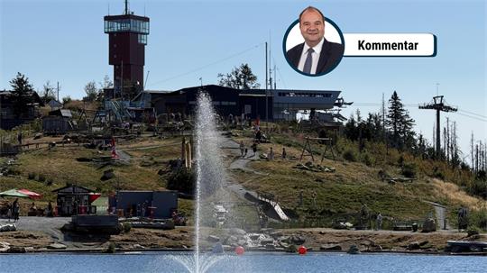 Das Foto zeigt einen Aussichtsturm auf einem Berg vor einem See mit einem Springbrunnen.