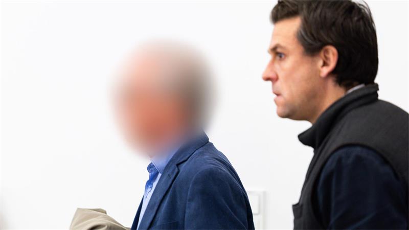 Zwei Männer betreten einen Gerichtssaal. Das Gesicht des Angeklagten ist verpixelt.