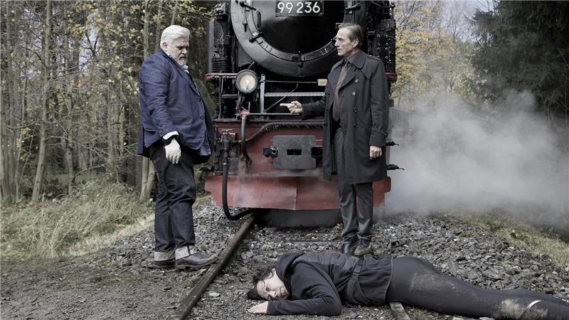 Dorfsheriff Frank Koops steht auf den Gleisen den der Brockenbahn, die auch im Hintergrund zu sehen ist. Daneben steht der erfahrene Ermittler Oliver Mienle. Vor beiden liegt die tote Beamtin Franziska Langer.