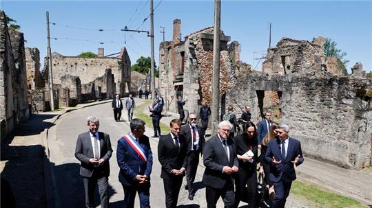 Der französische Präsident Emmanuel Macron und der deutsche Bundespräsident Frank-Walter Steinmeier gehen an Ruinen in Oradour-sur-Glane vorbei.