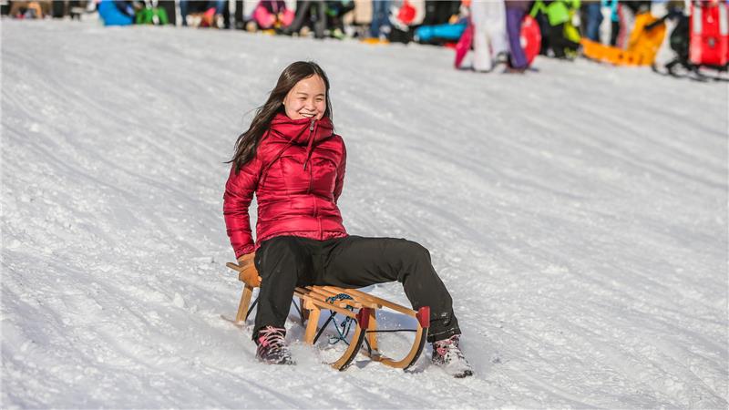 Das Foto zeigt ein Mädchen, das mit dem Schlitten den Hang hinab fährt.