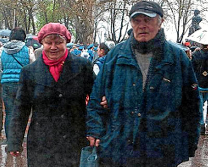 Tod in Odessa: Sohn eines Goslarer Zwangsarbeiterkindes stirbt Älteres Paar geht Arm in Arm auf einem nassen Weg, umgeben von mehreren Personen und Bäumen ohne Blätter.